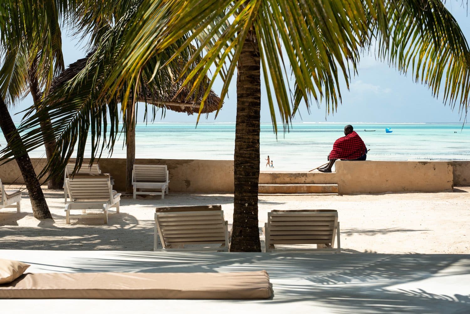 Strand am Casa Beach Hotel in Jambiani mit Liegen unter Palmen und Blick auf das flache, türkisfarbene Meer