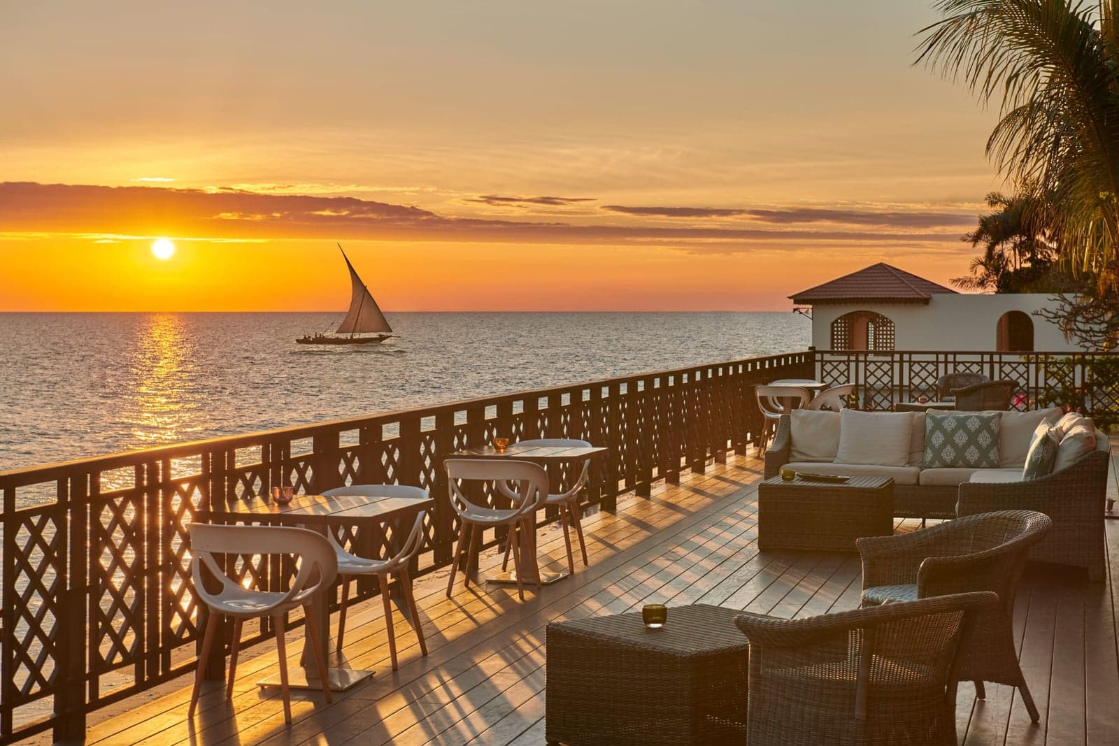 Restaurantterrasse an der Küste Sansibars bei Sonnenuntergang mit Dhow-Boot