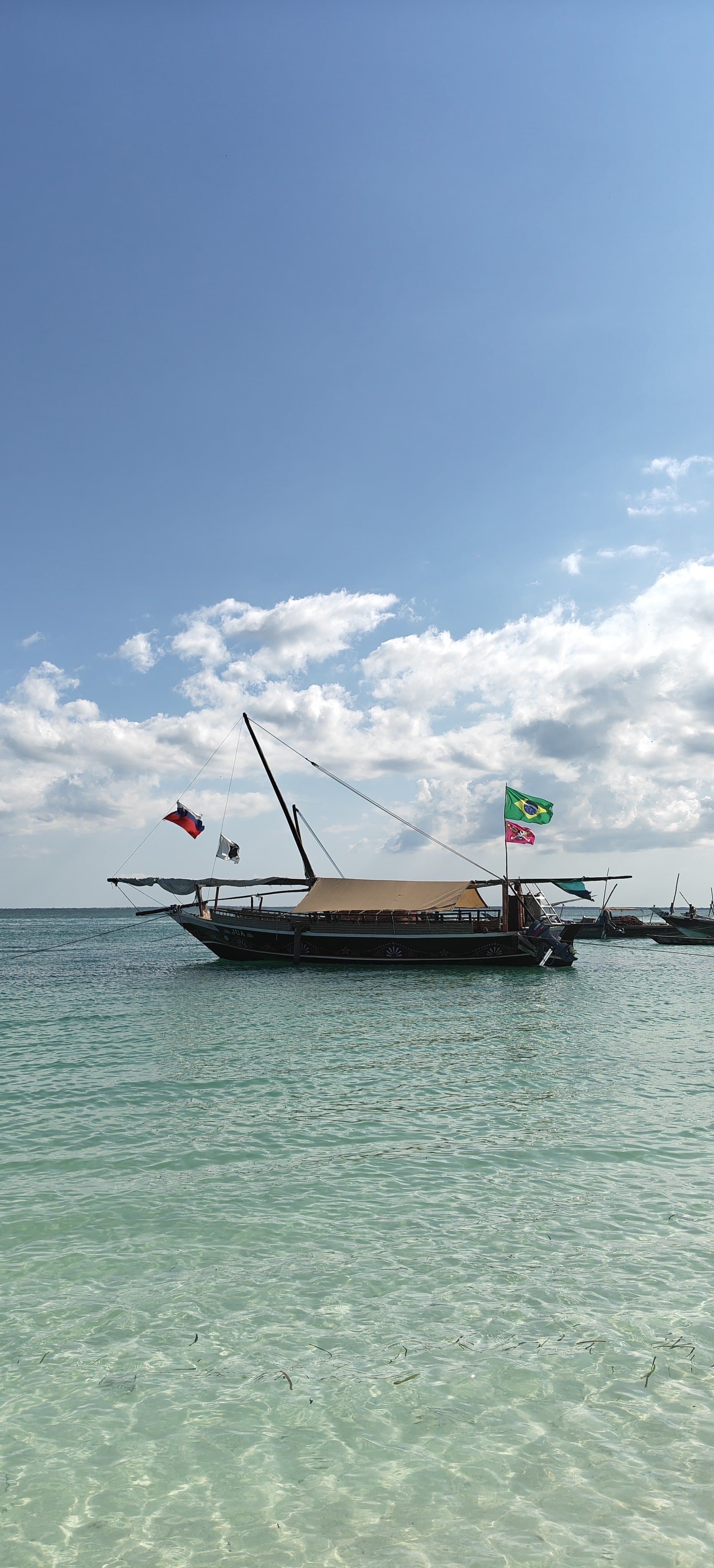 Dhau mit Flaggen im klaren, flachen Wasser vor dem Strand von Kendwa im Norden Sansibars