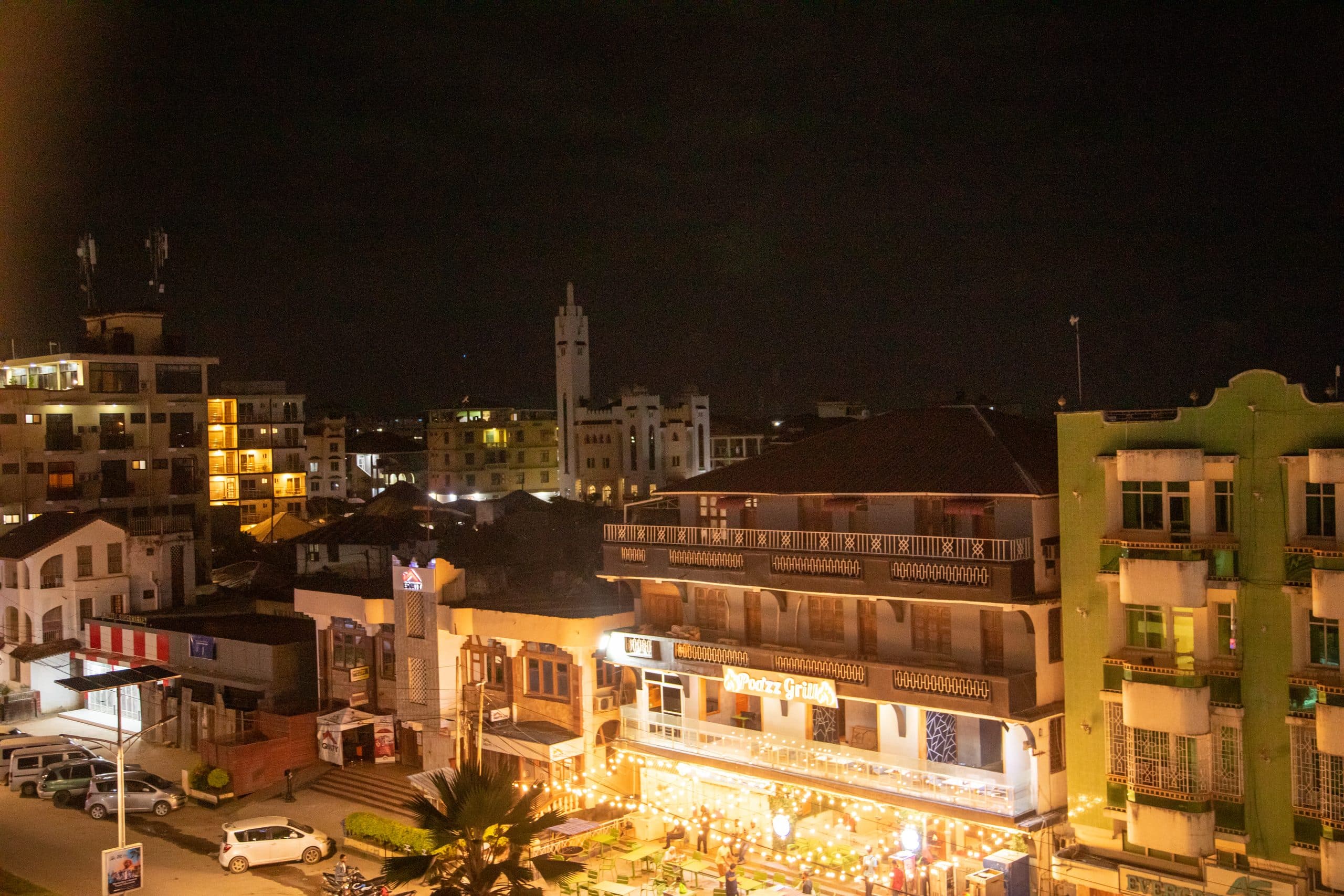 Blick über die beleuchteten Dächer von Stone Town am Abend, im Hintergrund ein Minarett