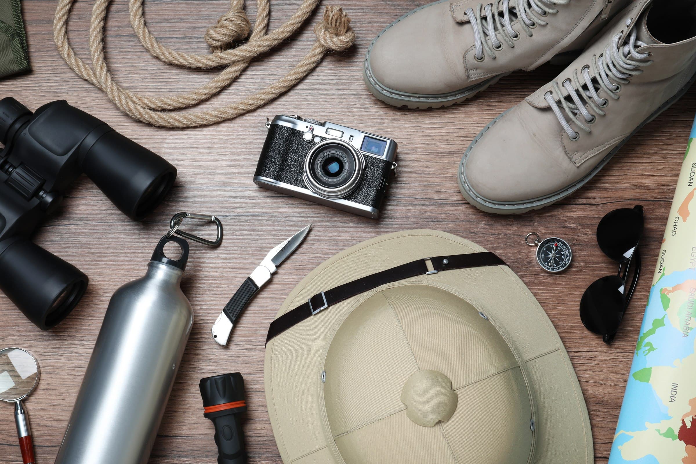 Safari-Ausrüstung im Flatlay: Hut, Fernglas, Kamera, Wanderstiefel und Kompass — die richtige Ausrüstung macht den Unterschied