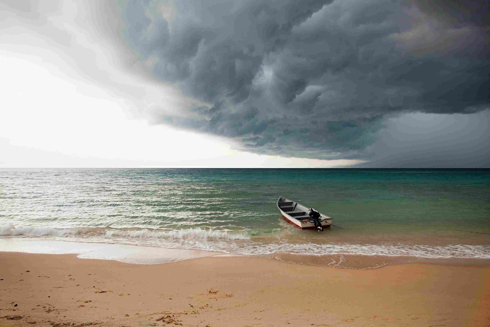 Dramatische Sturmwolken ziehen über einen Strand mit einem kleinen Fischerboot