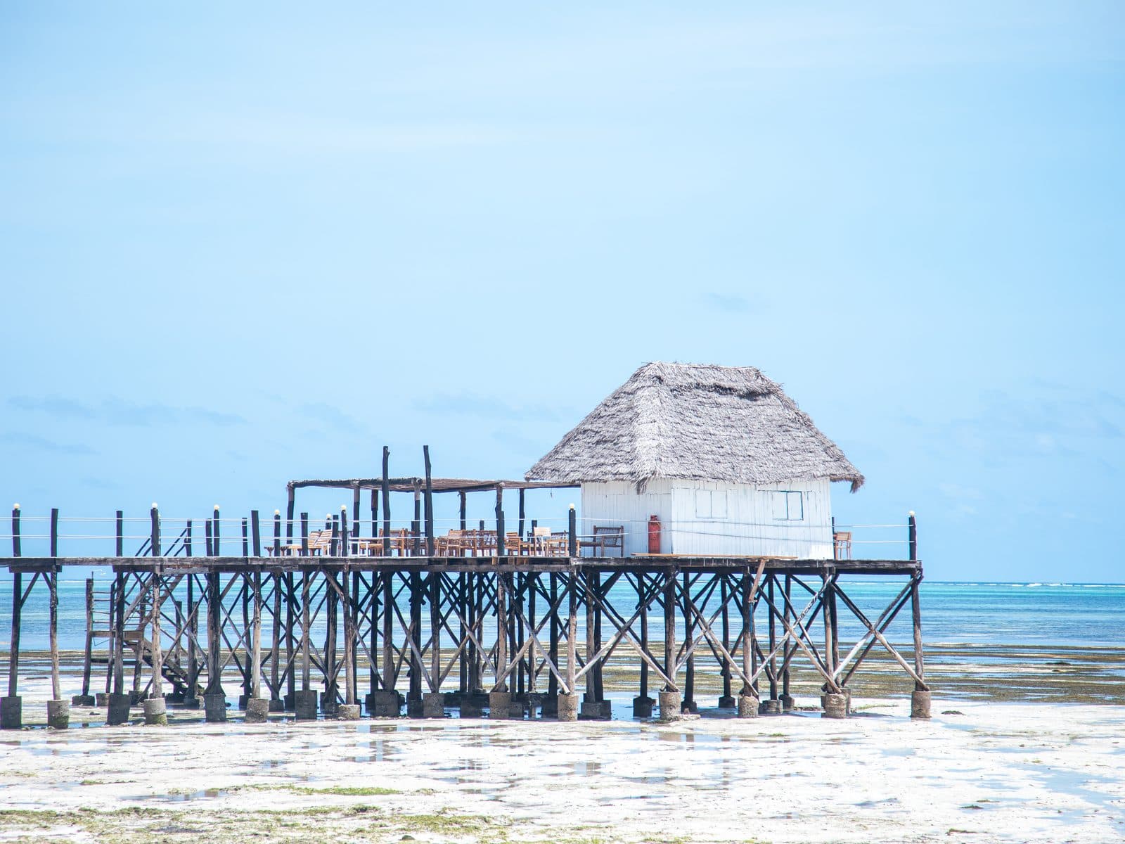 Holzsteg mit strohgedecktem Haus über dem Wasser bei Ebbe an der Küste Sansibars